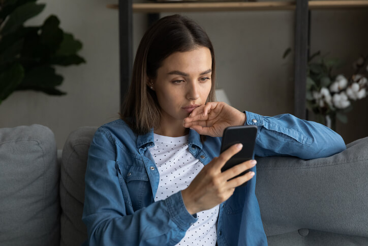 woman scrolling on phone while sitting on a sofa at home