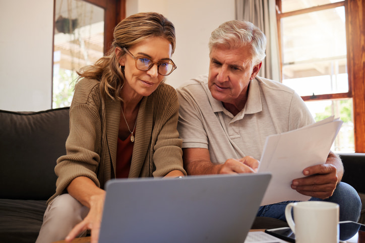 a middle aged couple sitting on a sofa looking at a laptop