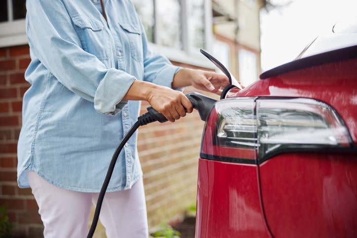 a woman charging an electric car on a driveway at home